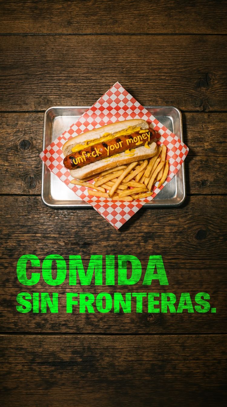 Perro caliente con papas fritas en una bandeja sobre una mesa de madera, bajo el lema Comida sin fronteras